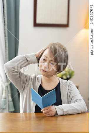 A senior woman looking at her pension book in the living room A senior woman looking at her pension book in the living room 140557971