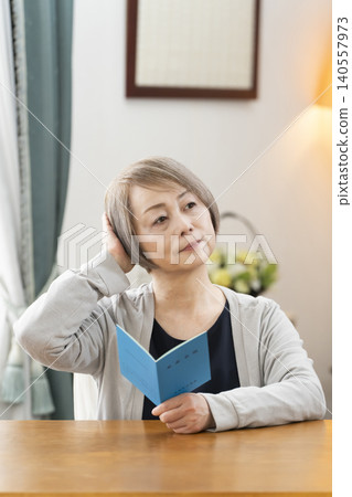 一位老婦人在客廳看著她的退休金手冊。 一位老婦人在客廳看著她的退休金手冊。 140557973