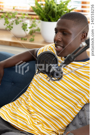 African american adult male sitting on couch at home studio speaking into condenser microphone African american adult male sitting on couch at home studio speaking into condenser microphone 140558256