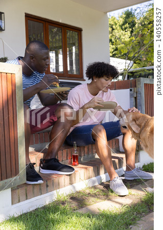Diverse male friends sitting on brick steps eating pizza slices, petting dog, with glass bottle Diverse male friends sitting on brick steps eating pizza slices, petting dog, with glass bottle 140558257