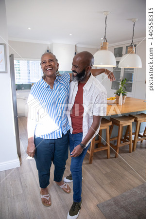 Senior African American mother and son hugging in modern kitchen with wooden island and fruit bowl Senior African American mother and son hugging in modern kitchen with wooden island and fruit bowl 140558315