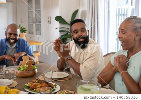 African American family sitting at kitchen table with lemonade pitcher roasted chicken, salad bowl African American family sitting at kitchen table with lemonade pitcher roasted chicken, salad bowl 140558316