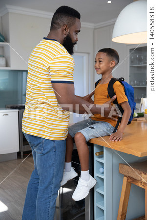African American father and son adjusting backpack straps on kitchen island next to fruit bowl African American father and son adjusting backpack straps on kitchen island next to fruit bowl 140558318