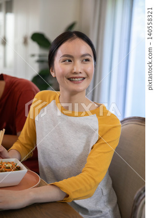 Asian friends sitting at wooden dining table eating noodles in bowl with chopsticks Asian friends sitting at wooden dining table eating noodles in bowl with chopsticks 140558321
