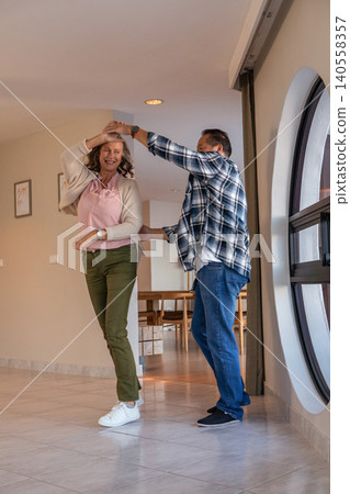Diverse couple dancing in hallway by round window and wooden dining table Diverse couple dancing in hallway by round window and wooden dining table 140558357