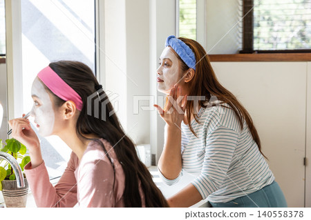 Asian mother and daughter applying facial masks and wearing colorful headbands at home vanity Asian mother and daughter applying facial masks and wearing colorful headbands at home vanity 140558378