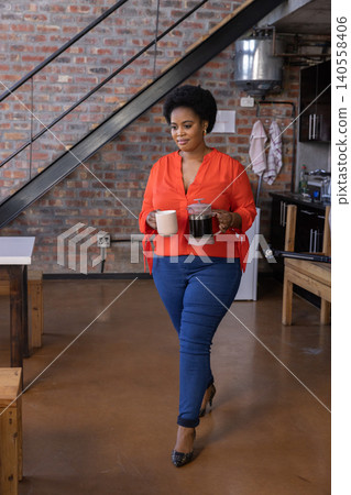 African american woman walking across loft-style kitchen with coffee mug and french press African american woman walking across loft-style kitchen with coffee mug and french press 140558406
