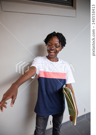 Teen african american male standing in school hallway holding notebooks in tee smiling Teen african american male standing in school hallway holding notebooks in tee smiling 140558413