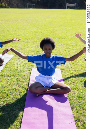 African american teen meditating cross-legged on mat on sports field near soccer goalposts African american teen meditating cross-legged on mat on sports field near soccer goalposts 140558422