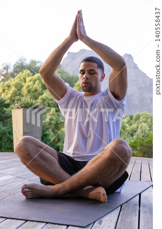 Hispanic man praying on yoga mat wearing sportswear beside planter holding succulents Hispanic man praying on yoga mat wearing sportswear beside planter holding succulents 140558437