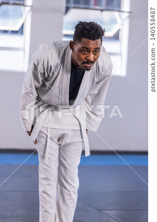 Adult african american male martial artist bowing in dojo in white gi and belt on mats Adult african american male martial artist bowing in dojo in white gi and belt on mats 140558487