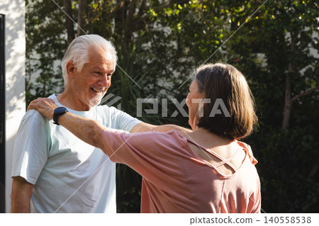 Senior couple dancing in sunlit garden with man wearing smartwatch and woman wearing pink blouse Senior couple dancing in sunlit garden with man wearing smartwatch and woman wearing pink blouse 140558538