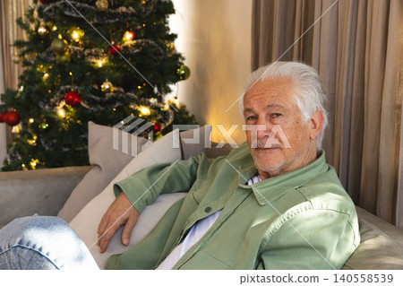 Senior man relaxing on sofa in living room beside Christmas tree with lights, baubles, copy space Senior man relaxing on sofa in living room beside Christmas tree with lights, baubles, copy space 140558539