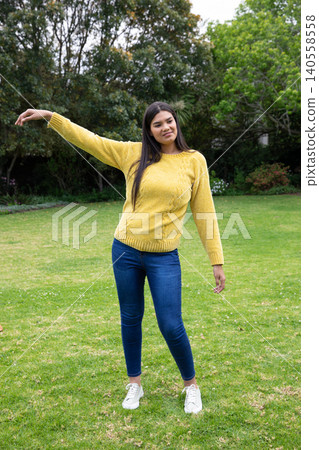 Asian woman wearing yellow knit sweater stretching arms on backyard garden lawn Asian woman wearing yellow knit sweater stretching arms on backyard garden lawn 140558558