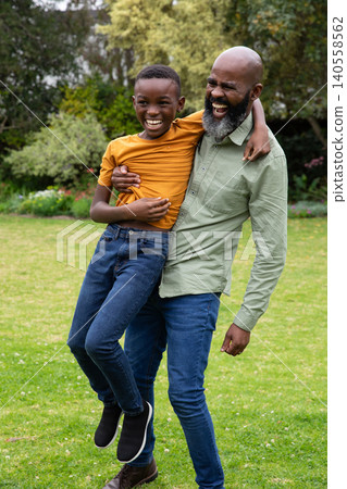 African american father and son lifting child and laughing in backyard garden with lawn African american father and son lifting child and laughing in backyard garden with lawn 140558562