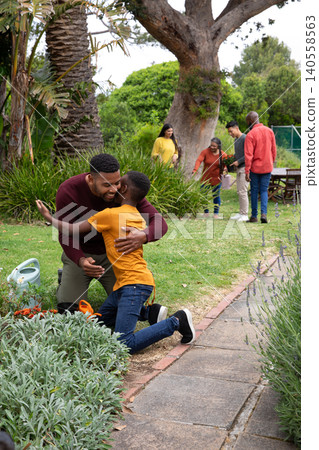 African american family hugging near brick-edged flower bed, using watering can in garden African american family hugging near brick-edged flower bed, using watering can in garden 140558563