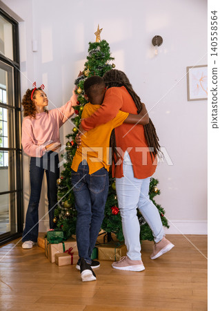 African american family decorating christmas tree in living room with gifts, reindeer headband 140558564