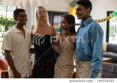 Diverse friends posing together in living room with paper bunting, balloon clusters Diverse friends posing together in living room with paper bunting, balloon clusters 140558585