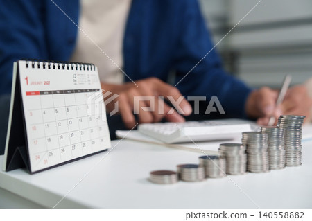 Person calculating finance budget savings with calendar and coins on desk Person calculating finance budget savings with calendar and coins on desk 140558882