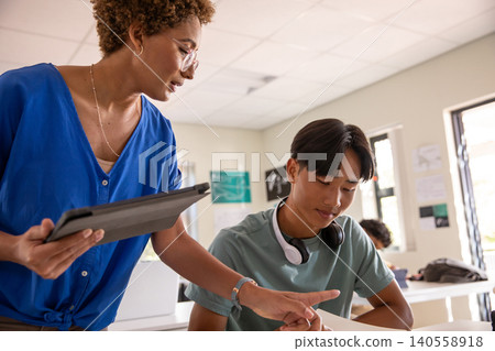 Female teacher and asian teen student wearing headphones holding tablet pointing at papers Female teacher and asian teen student wearing headphones holding tablet pointing at papers 140558918