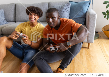 Diverse male friends playing games on floor against couch in living room using controllers Diverse male friends playing games on floor against couch in living room using controllers 140558919