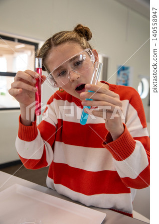 Female child science student examining red, blue test tubes at lab bench with safety goggles Female child science student examining red, blue test tubes at lab bench with safety goggles 140558947