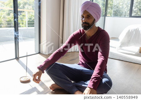Indian man meditating cross-legged on hardwood bedroom floor near burning incense holder Indian man meditating cross-legged on hardwood bedroom floor near burning incense holder 140558949