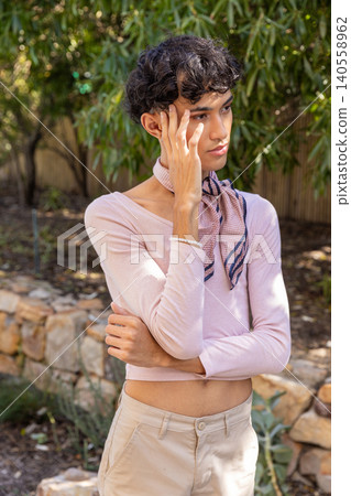 Man with arms crossed and hand to face in backyard by stone wall wearing scarf, bracelet Man with arms crossed and hand to face in backyard by stone wall wearing scarf, bracelet 140558962