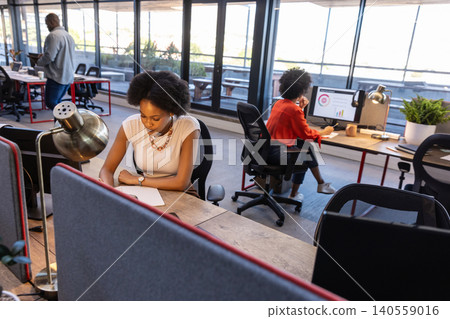 Diverse coworkers writing and viewing charts in office using notepad, computer and smartphone Diverse coworkers writing and viewing charts in office using notepad, computer and smartphone 140559016