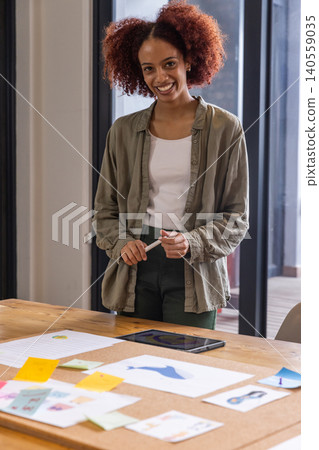 African american woman smiling while holding marker at table with sketches, tablet in studio African american woman smiling while holding marker at table with sketches, tablet in studio 140559035