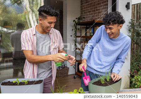 Diverse male friends gardening on deck table planting seedlings with spray bottle, trowel Diverse male friends gardening on deck table planting seedlings with spray bottle, trowel 140559043