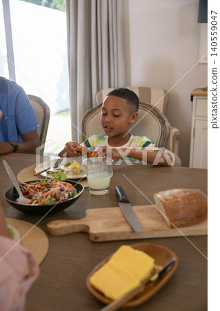 African American family eating at dining table with chicken drumstick salad bowl glass of milk African American family eating at dining table with chicken drumstick salad bowl glass of milk 140559047