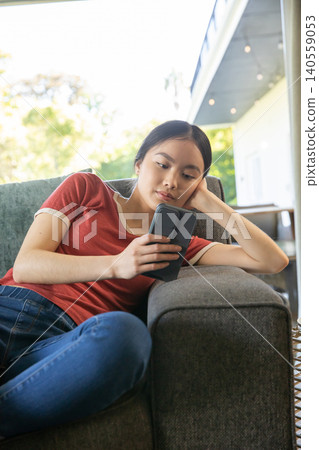 Asian woman reclining on upholstered sofa on covered porch and using smartphone Asian woman reclining on upholstered sofa on covered porch and using smartphone 140559053