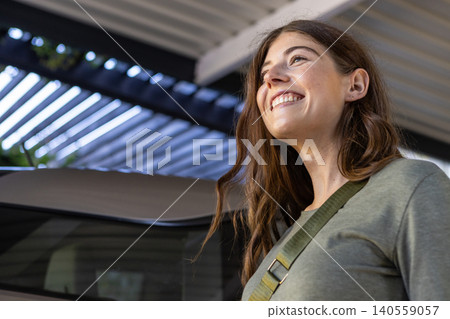 Woman standing under metal beams at parking structure next to car, wearing crossbody strap Woman standing under metal beams at parking structure next to car, wearing crossbody strap 140559057