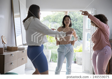 Diverse female friends practicing dance moves by sliding glass door in bright living room Diverse female friends practicing dance moves by sliding glass door in bright living room 140559075