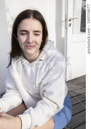 Female sitting on wooden deck wearing white hoodie and blue skirt showing silver hoop earrings Female sitting on wooden deck wearing white hoodie and blue skirt showing silver hoop earrings 140559077