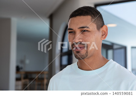 African American man posing in living area wearing white Tshirt near dining table chairs copy space African American man posing in living area wearing white Tshirt near dining table chairs copy space 140559081