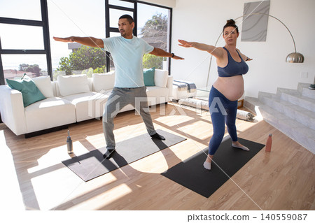 Friends practicing warrior II yoga pose on mats in bright living room with water bottles Friends practicing warrior II yoga pose on mats in bright living room with water bottles 140559087