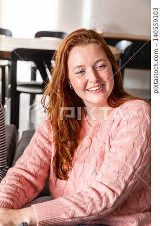 Female friends smiling and leaning while conversing in modern lounge on gray sofa Female friends smiling and leaning while conversing in modern lounge on gray sofa 140559103