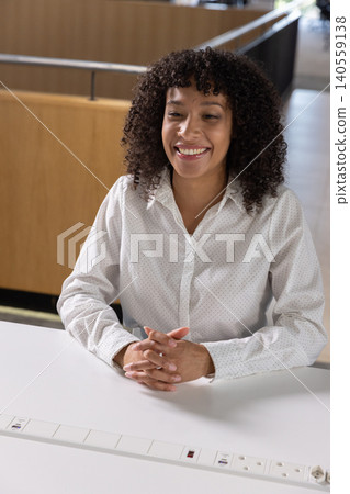 African american woman sitting at white desk in workspace in dotted shirt using power outlet African american woman sitting at white desk in workspace in dotted shirt using power outlet 140559138