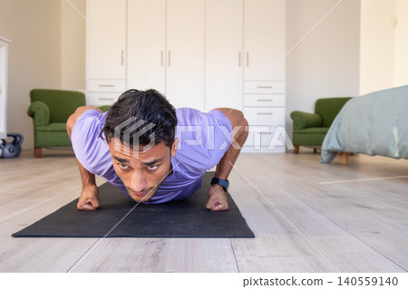 Asian man performing low push-up on exercise mat in home workout area with kettlebell Asian man performing low push-up on exercise mat in home workout area with kettlebell 140559140