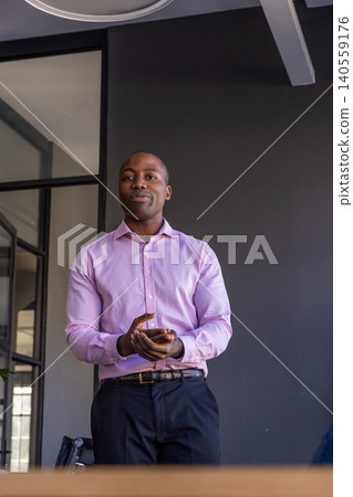 African american man standing behind meeting table holding smartphone in office African american man standing behind meeting table holding smartphone in office 140559176