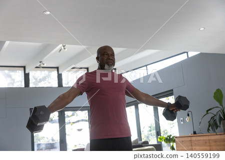 Senior african american man lifting dumbbells in living room with glass doors and plants Senior african american man lifting dumbbells in living room with glass doors and plants 140559199
