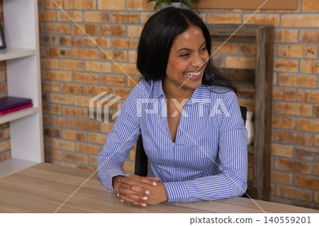 African american woman in striped shirt sitting at office desk smiling and talking 140559201