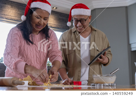 Diverse senior couple in santa hats preparing dough at kitchen countertop with tablet Diverse senior couple in santa hats preparing dough at kitchen countertop with tablet 140559249