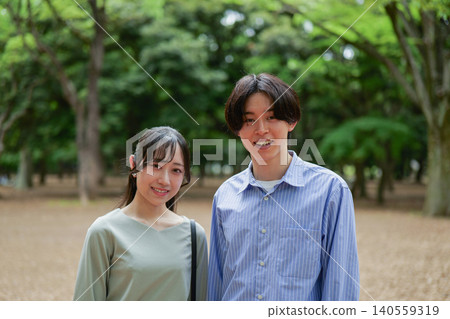 一對年輕夫婦在鬱鬱蔥蔥的樹木背景下微笑的肖像。 一對年輕夫婦在鬱鬱蔥蔥的樹木背景下微笑的肖像。 140559319