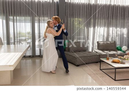 Bride and groom dancing in modern reception space with sheer gray curtains, table, balloons Bride and groom dancing in modern reception space with sheer gray curtains, table, balloons 140559344
