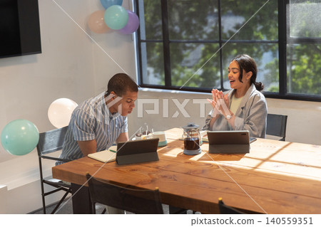 Diverse colleagues celebrating birthday at office table, tablets, cake, french press, balloons Diverse colleagues celebrating birthday at office table, tablets, cake, french press, balloons 140559351