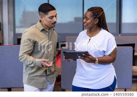 Diverse coworkers collaborating on digital tablet at office near partitioned desks, dividers Diverse coworkers collaborating on digital tablet at office near partitioned desks, dividers 140559380