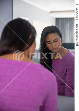 Asian woman sitting in home dressing area in magenta top and gazing into wall-mounted mirror Asian woman sitting in home dressing area in magenta top and gazing into wall-mounted mirror 140559401